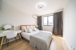 Un dormitorio con cama, escritorio, espejo y ventana con cortinas.