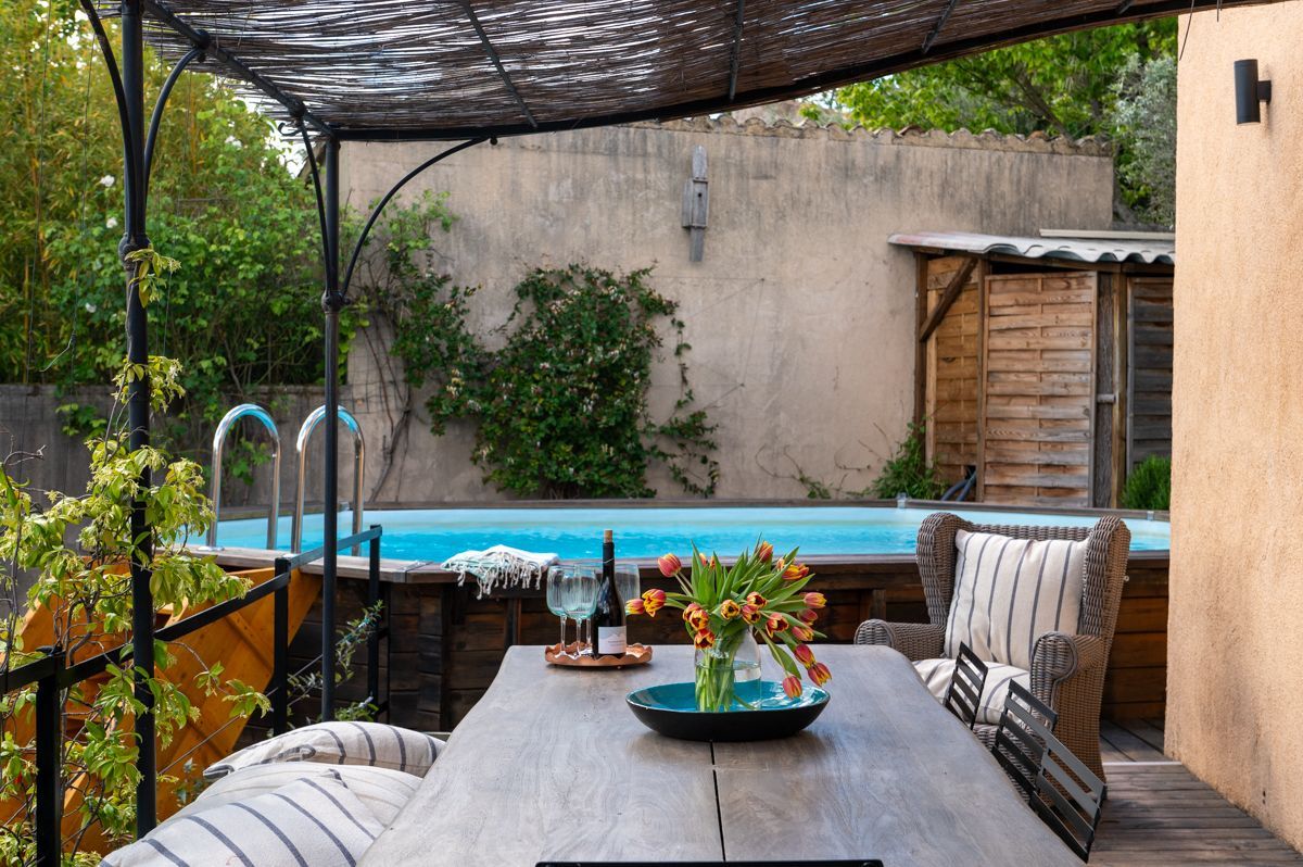 An outdoor patio with a pool, a table with a vase of flowers, and wicker furniture.
