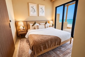 A bedroom with a large bed, bedside lamps, a view of the ocean, and two framed botanical prints on the wall. - Western Beach Resort (Al Sila)