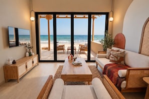 A modern living room with a large sliding glass door leading to a beach view, furnished with a sofa, coffee table, and a TV. - Western Beach Resort (Al Sila)