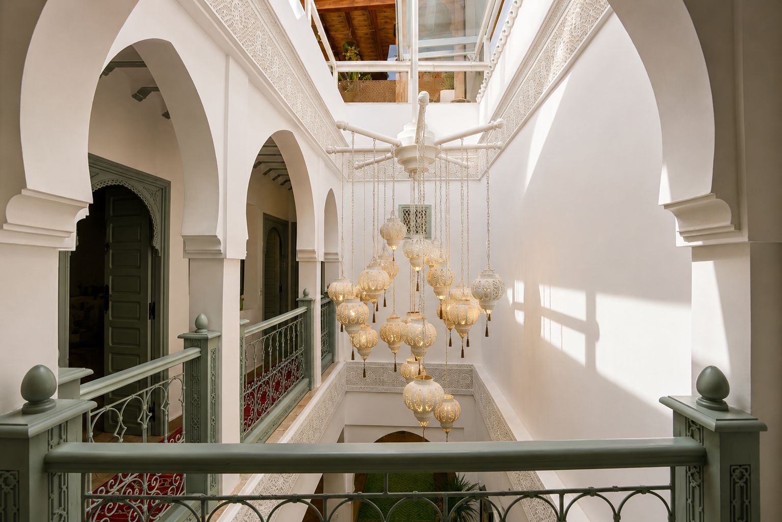 A corridor with white arches, a hanging chandelier, and a balcony railing.