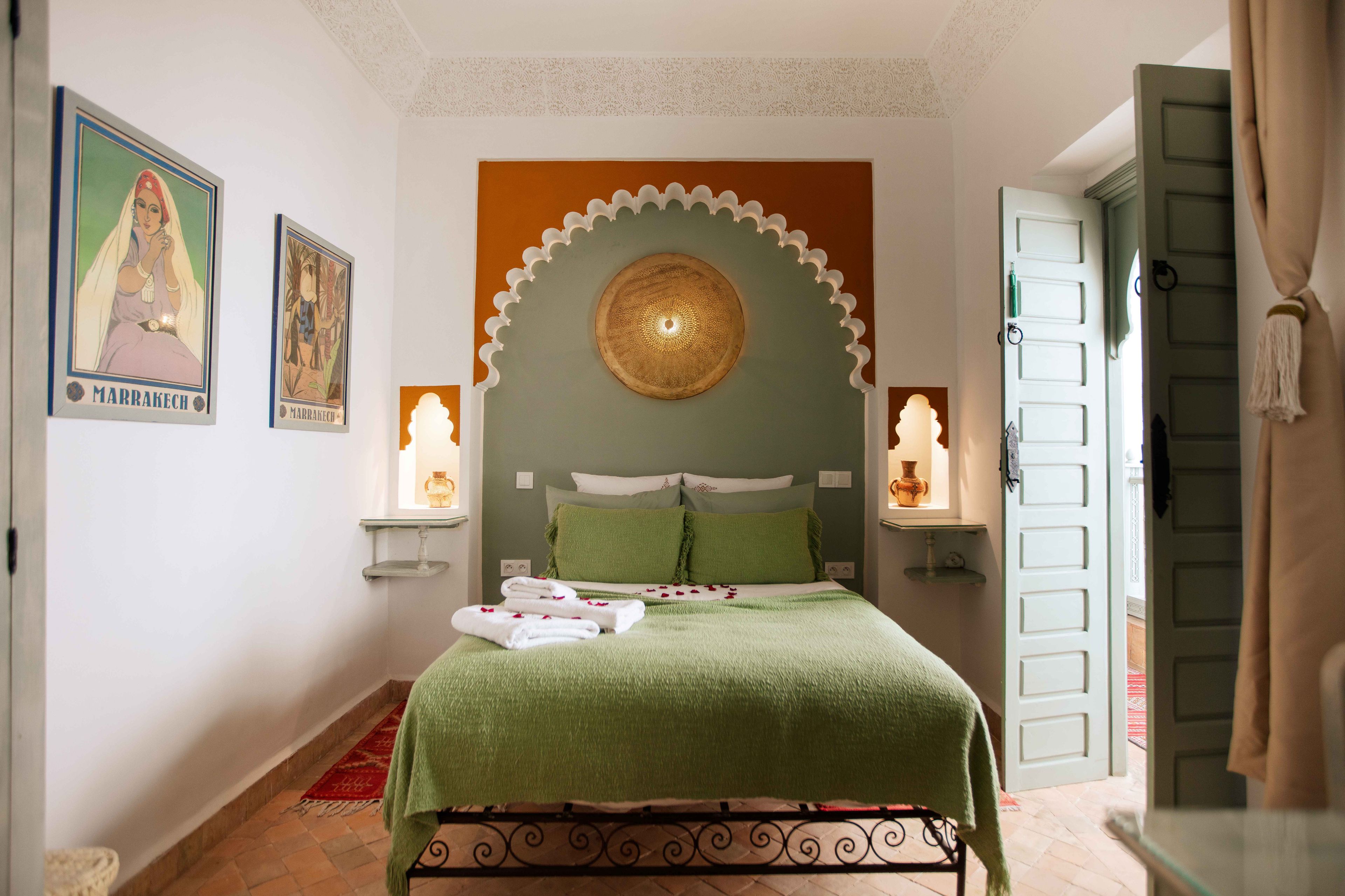 A neatly made bed with a green bedspread and white pillows, flanked by two wall-mounted lamps.