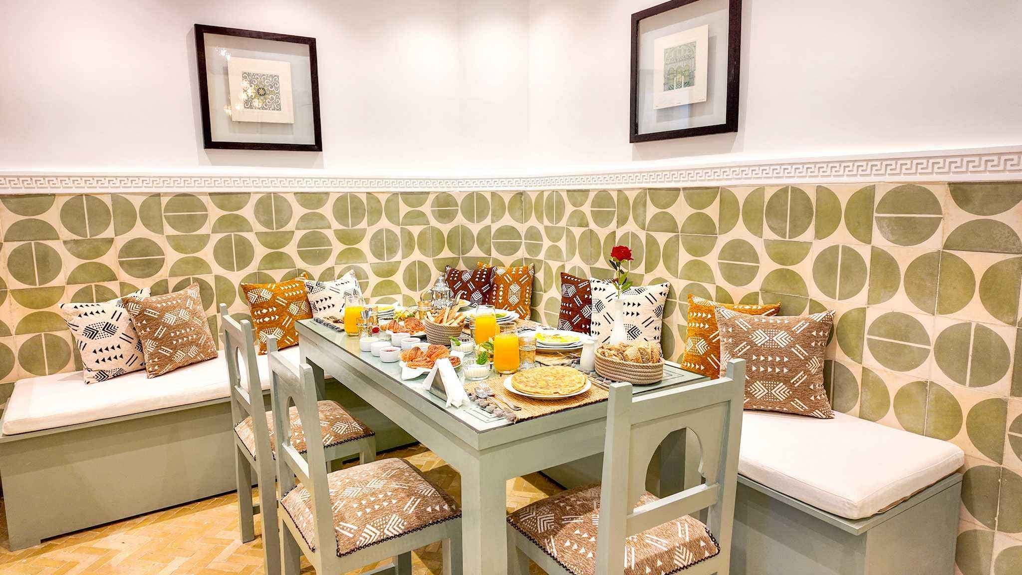 A dining area with a table set for breakfast, including bread, pastries, and a fruit bowl.