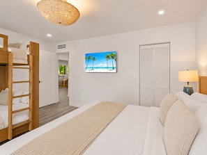 A hotel room with a bunk bed, a flat-screen TV, a wardrobe, and a bedside lamp. - Renovated PGA National Home by Guaranteed Rental (Palm Beach Gardens)