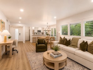 A modern living room with a sofa, coffee table, and a dining area with a kitchen in the background. - Renovated PGA National Home by Guaranteed Rental (Palm Beach Gardens)