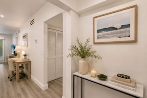 A hallway with a desk, a plant, a framed picture, and a book on a console table. - Renovated PGA National Home by Guaranteed Rental (Palm Beach Gardens)