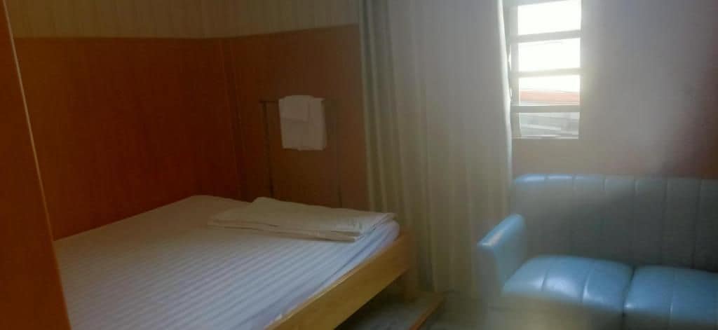 A single bed with a wooden headboard, a small table, and a chair in a room with a window.