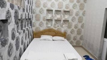 A bedroom with a bed, a wall-mounted fan, an air conditioning unit, and patterned wallpaper.