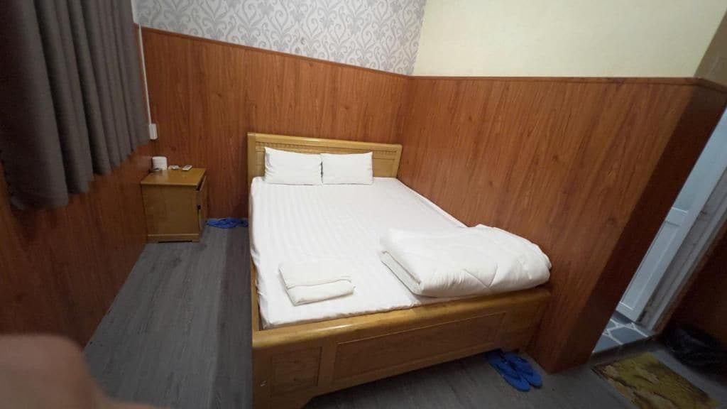 Un lit simple avec une tête de lit en bois, dans une pièce dont le papier peint est à motifs et qui possède un mur recouvert de panneaux en bois.