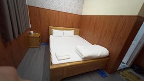 Ein Einzelbett mit Holz-Kopfstück in einem Zimmer mit strukturiertem Wandpapier und einer Holzvertäfelung.