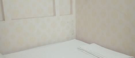 Una cama individual con estructura de madera y colchón blanco en una habitación con paredes lisas y piso de color claro.