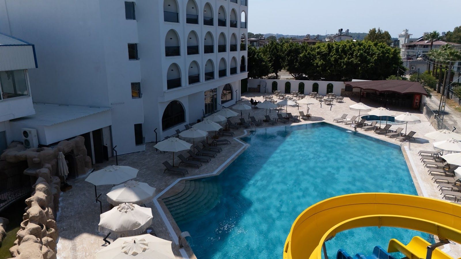 Área de piscina de hotel com piscina grande, espreguiçadeiras, guarda-sóis e um tobogã.