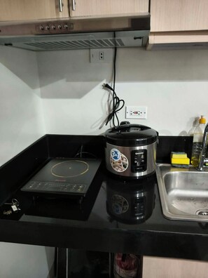 A compact kitchen with a built-in induction cooktop, a rice cooker, and a stainless steel sink. - Your Cozy Nest in Novaliches-SMDC Hills Residences Novaliches (Quezon City)