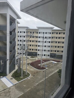 A multi-story residential building with balconies, a parking area, and utility poles. - Your Cozy Nest in Novaliches-SMDC Hills Residences Novaliches (Quezon City)