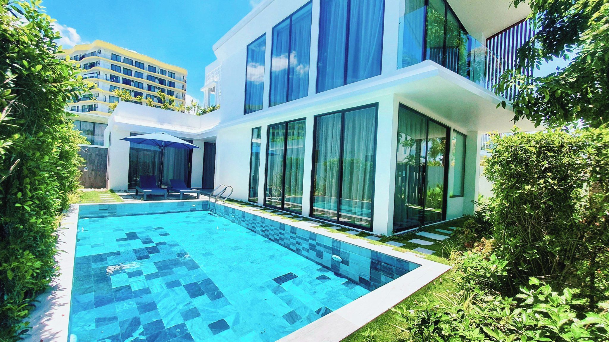 Um edifício residencial moderno com piscina, grandes janelas e um jardim bem cuidado.