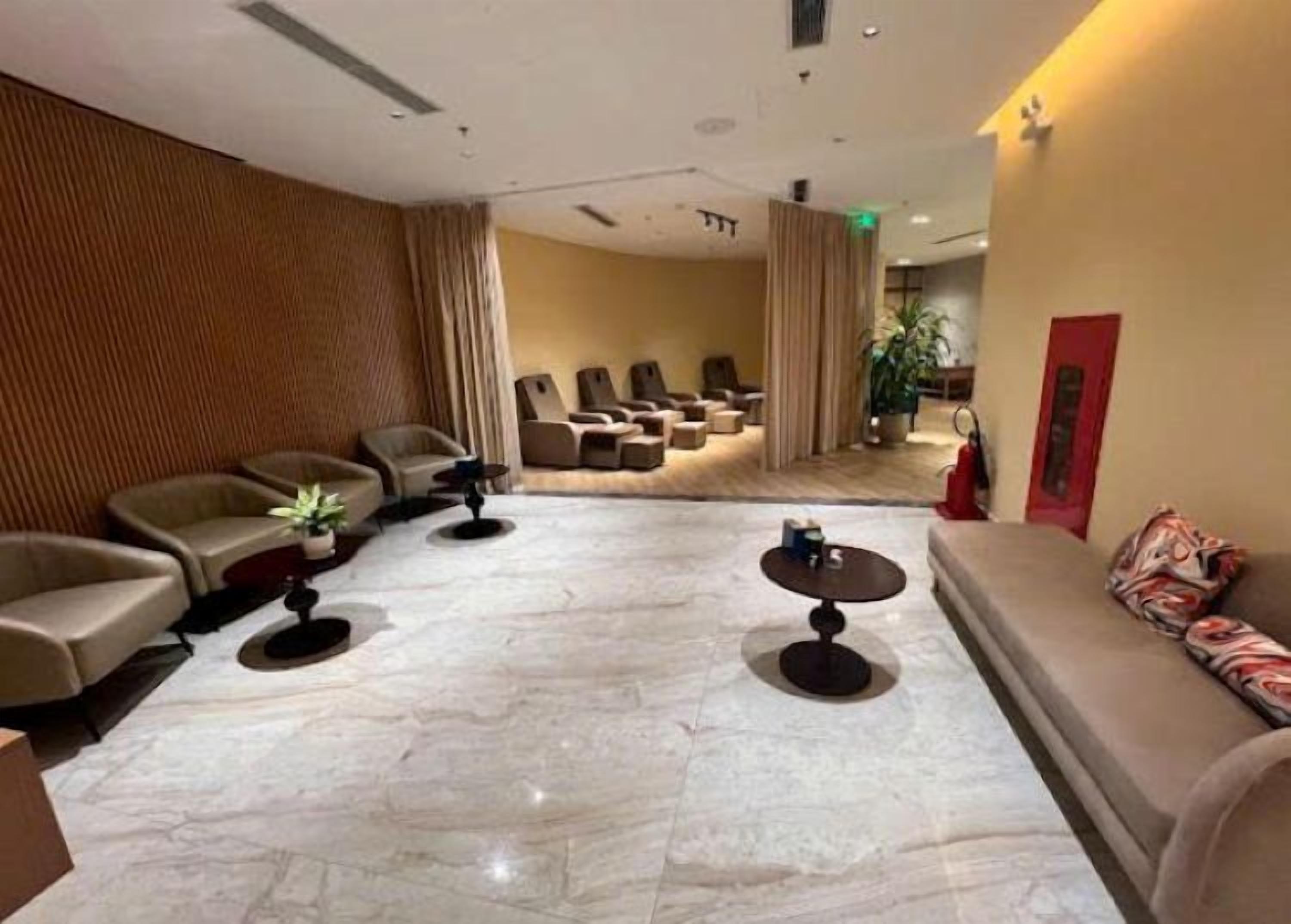 Um hall de hotel com áreas de estar, balcão de recepção e uma porta vermelha.