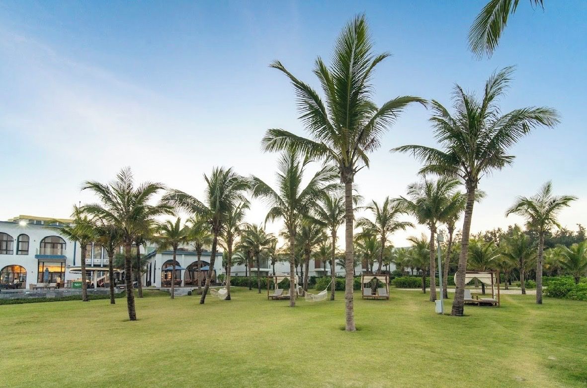 Un resort con palmeras, césped y un edificio con ventanas arqueadas.