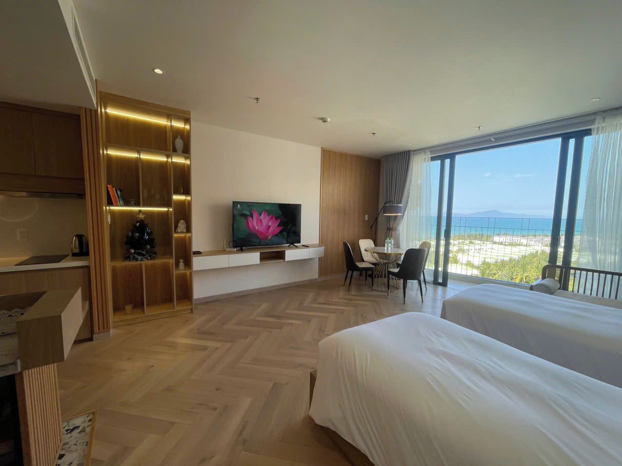 A hotel room with a large bed, a TV, a desk, and a view of the ocean.