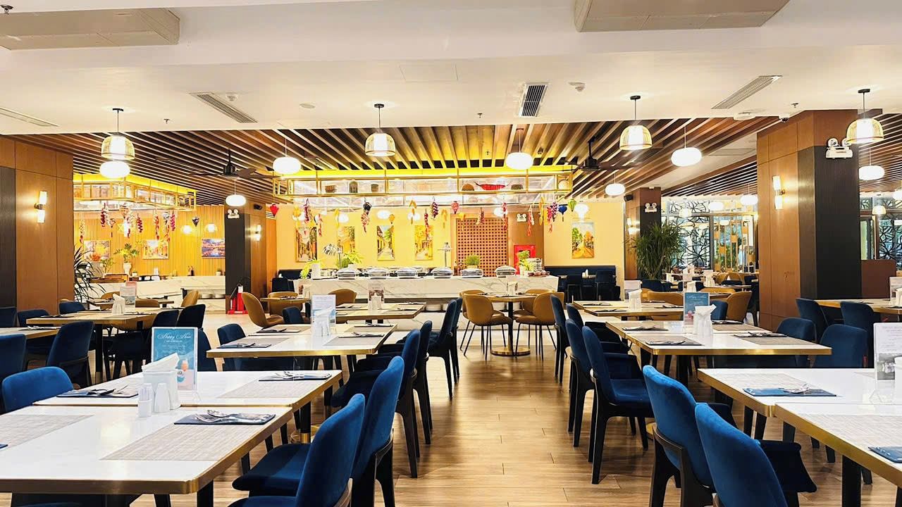 Um restaurante com várias mesas e cadeiras, teto de madeira e luminárias pendentes.