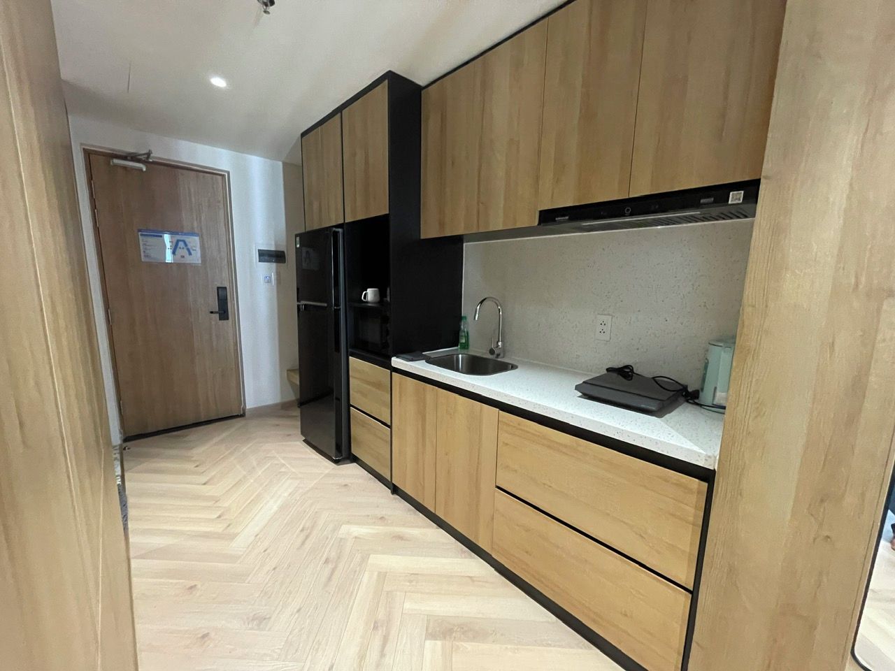 A modern kitchen with wooden cabinets, a black refrigerator, a stainless steel sink, and a countertop with a kettle.