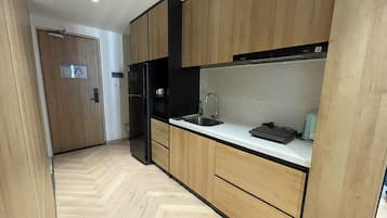 A modern kitchen with wooden cabinets, a black refrigerator, a stainless steel sink, and a countertop with a kettle.