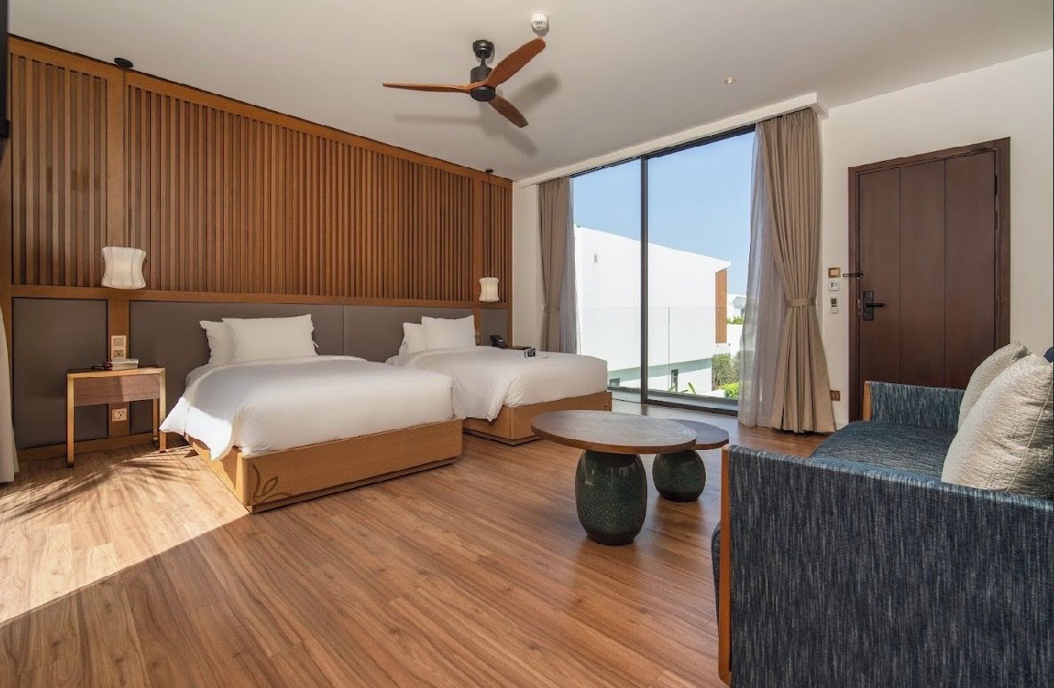 Una habitación de hotel con dos camas, un sofá, un ventilador de techo y un ventanal grande.