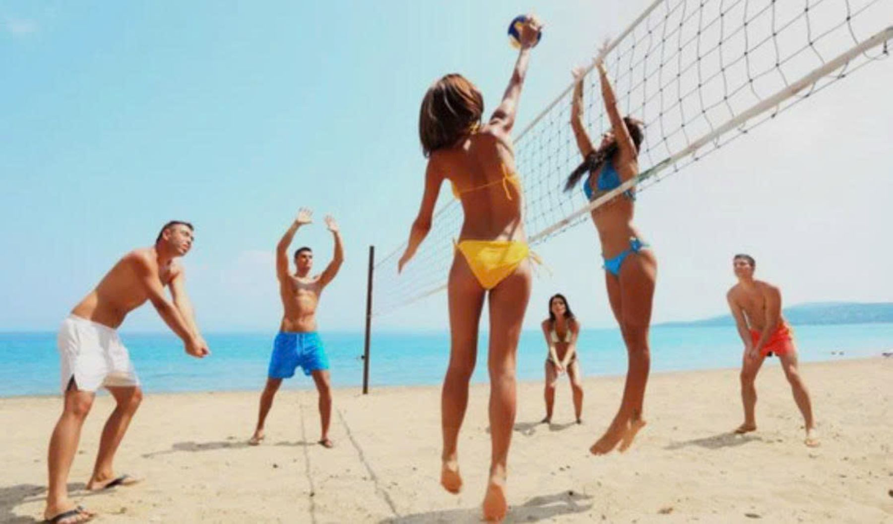 A beach volleyball game with players in swimwear.