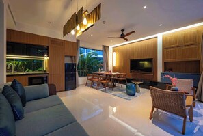 Una sala de estar moderna con sofá, mesa de comedor, sillas, televisión y una cocina con refrigerador y microondas.