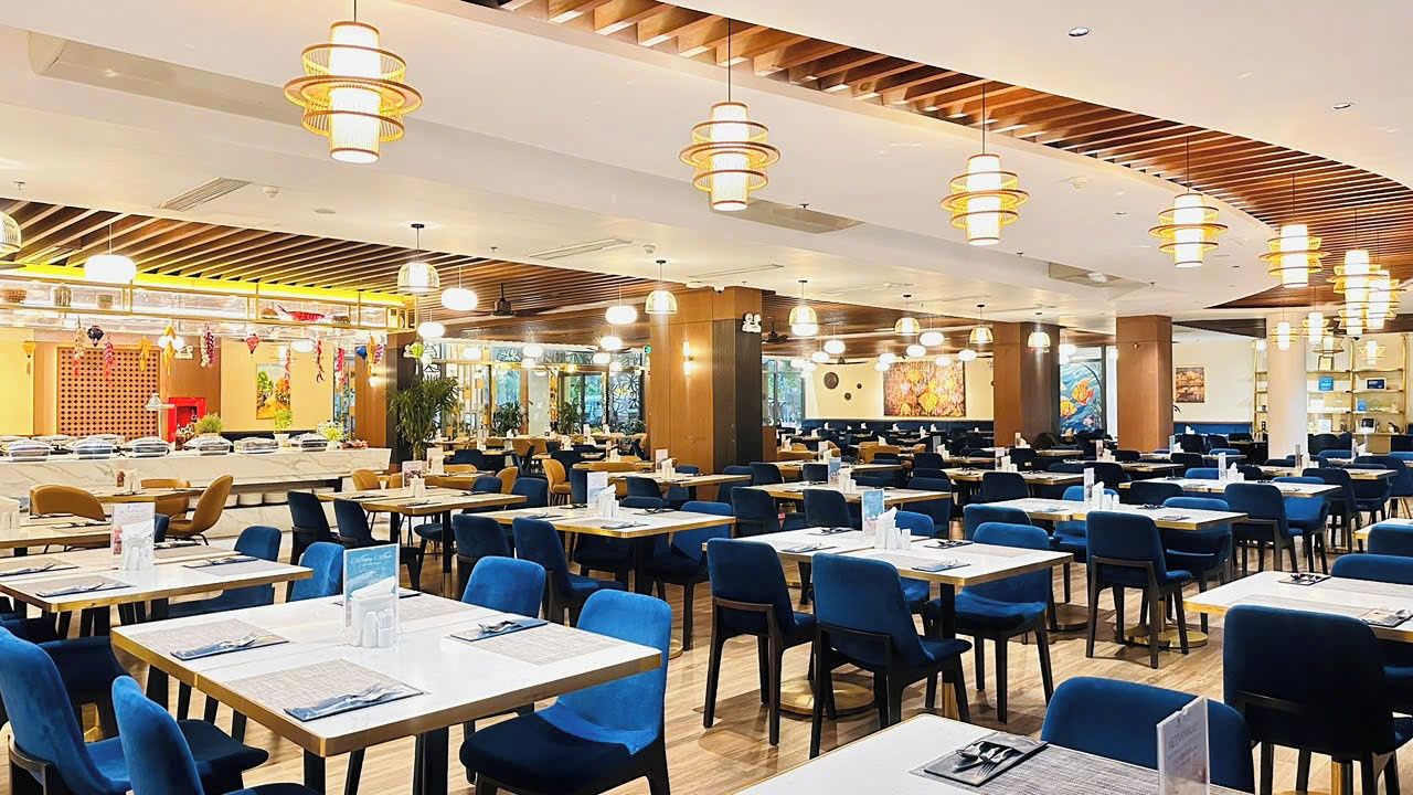 Un restaurante espacioso con numerosas mesas y sillas, con una decoración interior moderna y lámparas colgantes.