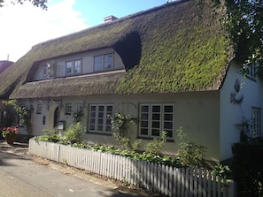 A traditional house with a thatched roof, white exterior walls, and a white picket fence. - "reetstubchen" - House Shell (Nieblum)
