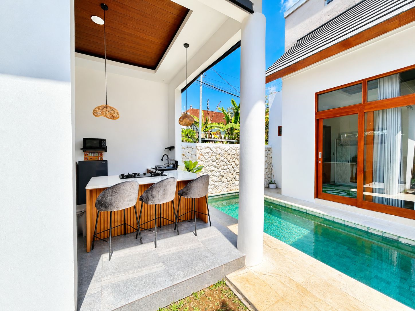 Eine moderne Außenküche mit einer Steinwand, einer Sitzgruppe am Pool und einer großen Glasschiebetür zum Pool.