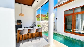 Eine moderne Außenküche mit einer Steinwand, einer Sitzgruppe am Pool und einer großen Glasschiebetür zum Pool.