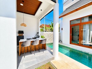 Eine moderne Außenküche mit einer Steinwand, einer Sitzgruppe am Pool und einer großen Glasschiebetür zum Pool.