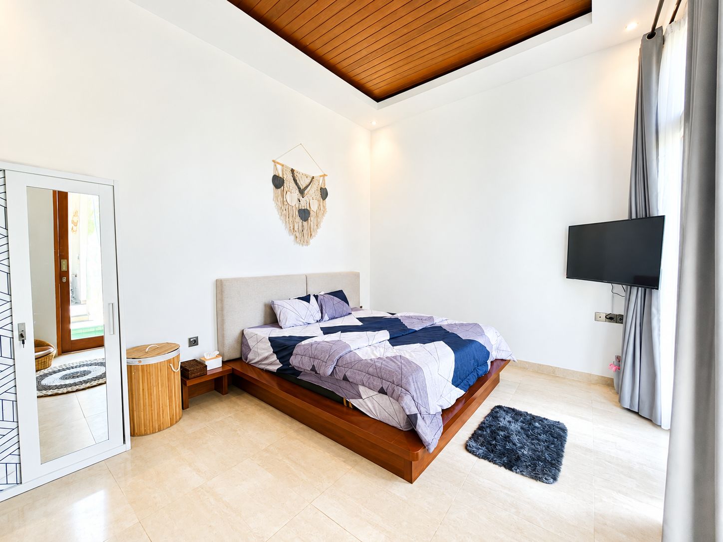 Une chambre à coucher moderne, équipée d’un lit, d’une télévision, d’un miroir et d’un plafond avec des poutres en bois.
