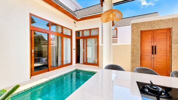 A modern pool area with glass doors, a dining table, and a stove.
