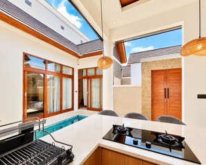 A modern kitchen with a built-in gas stove, a bar area with a grill, and a poolside seating area.
