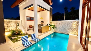 Ein moderner Poolbereich im Freien mit Bar und Sitzgelegenheiten, umgeben von einer Steinmauer und einer Holzterrasse.