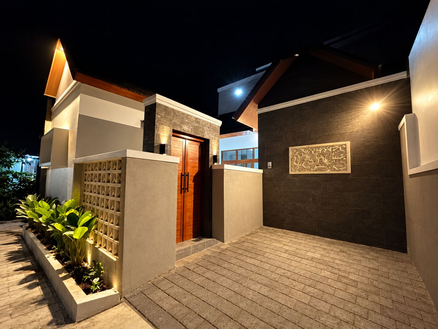 A modern house with a wooden door, a dark wall with a decorative panel, and a brick pathway.