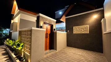 A modern house with a wooden door, a dark wall with a decorative panel, and a brick pathway.