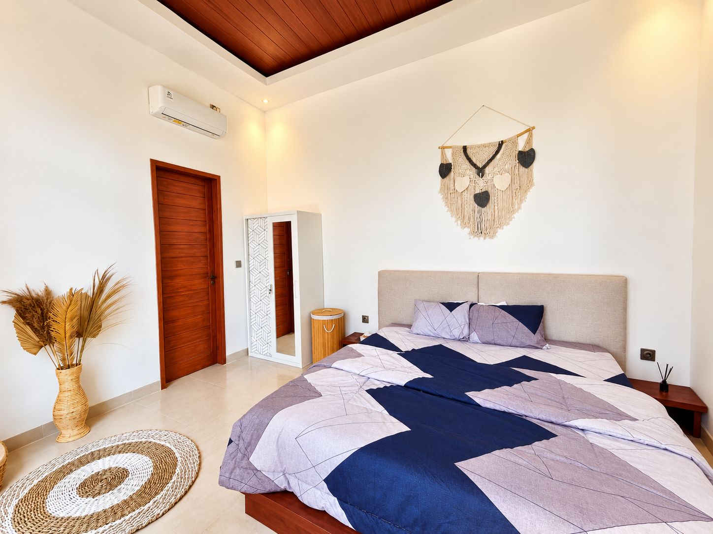 Quarto com cama, porta de madeira, ar-condicionado fixado na parede, um objeto decorativo na parede e um tapete redondo tecido.