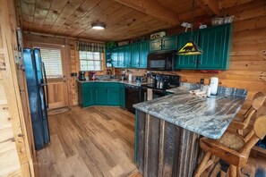 A kitchen with wooden cabinets, a refrigerator, a microwave, and a granite countertop. - Awestruck: Hot Tub, Pool Access, Perfect Mountain Views, & Fireplace (Sevierville)