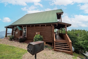 Eine Holzhütte mit einem grünen Dach, einer Veranda und einem Grillplatz.