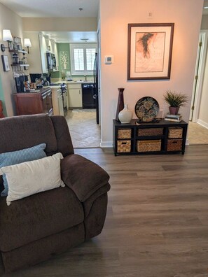 Ein Wohnzimmer mit einem braunen Sofa, einem Beistelltisch mit Dekoration und einer Küche im Hintergrund.