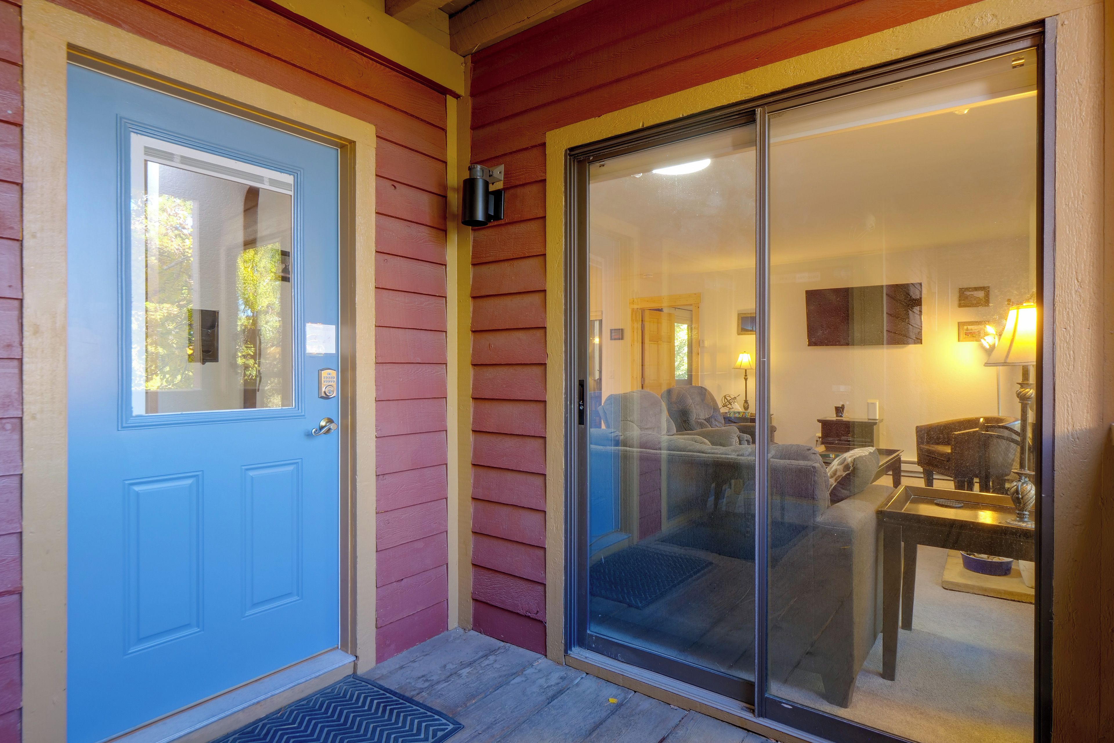 A blue door with a keypad lock, a sliding glass door, and a small porch area with a doormat.