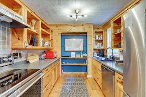 A modern kitchen with wooden cabinetry, stainless steel appliances, and a blue accent wall. - Cabin w/ Hot Tub, Near Mercier Orchard & Downtown (Blue Ridge)