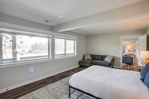 A bedroom with a bed, a gray sofa, and a view of a lake through large windows. - Dock Access, Deck & BBQ on Liberty Lake (Liberty Lake)