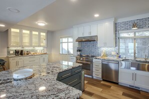 A modern kitchen with white cabinetry, a granite countertop, stainless steel appliances, and a herringbone tile backsplash. - Liberty Lake Retreat w/ Private Dock (Liberty Lake)