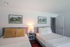 Een hotelkamer met twee bedden, een nachtkastje met lamp en twee lijstwerken met landschappen aan de muur.