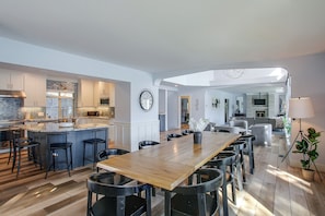 A spacious kitchen with modern appliances, a dining area with a long wooden table, and a living room with a sofa and a TV. - Liberty Lake Retreat w/ Private Dock (Liberty Lake)