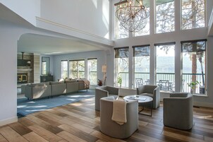 A spacious living area with a high ceiling, large windows, and a modern chandelier.